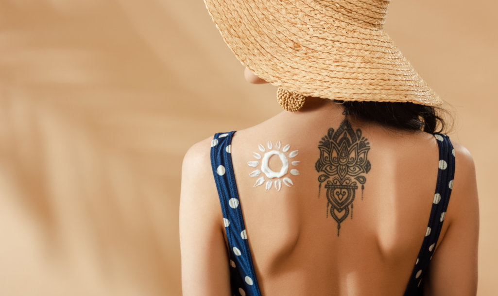 woman in polka dot swimsuit and straw hat with drawn sun and tattoo on back on beige background