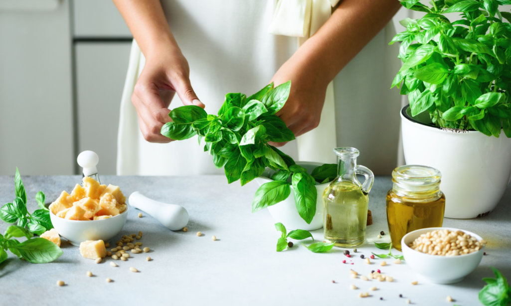 Woman in oversize dress holding pot with fresh organic basil, white kitchen interior design