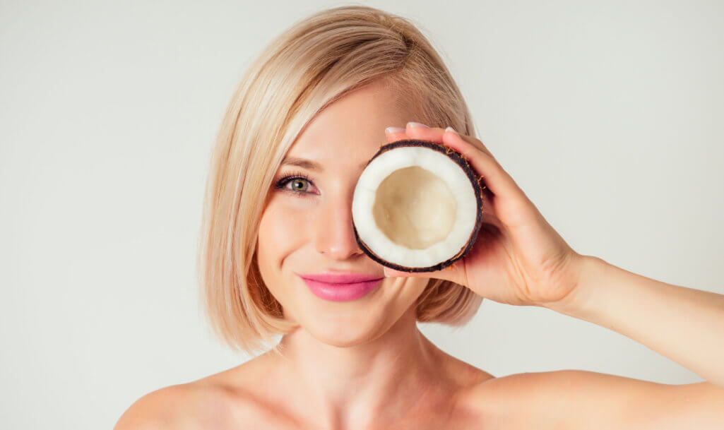 Beautiful young blonde hairstyle girl with a long eyelashes make-up and perfect skin with coconut in her hand in the studio on a white background