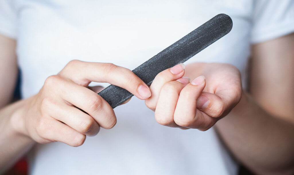 The girl aligns her nails with a nail file.