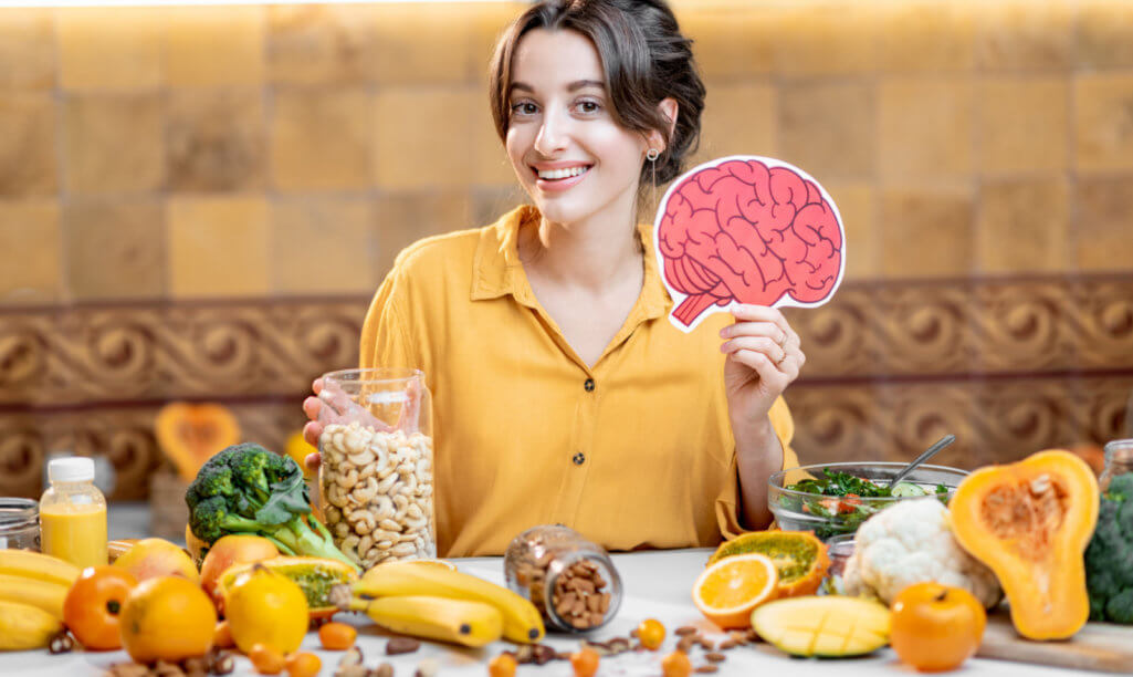 Woman holding human brain model with variety of healthy fresh food on the table. Concept of balanced nutrition for brain health