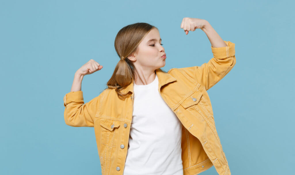 Strong little blonde kid girl 12-13 years old in yellow jacket posing isolated on blue background children studio portrait.