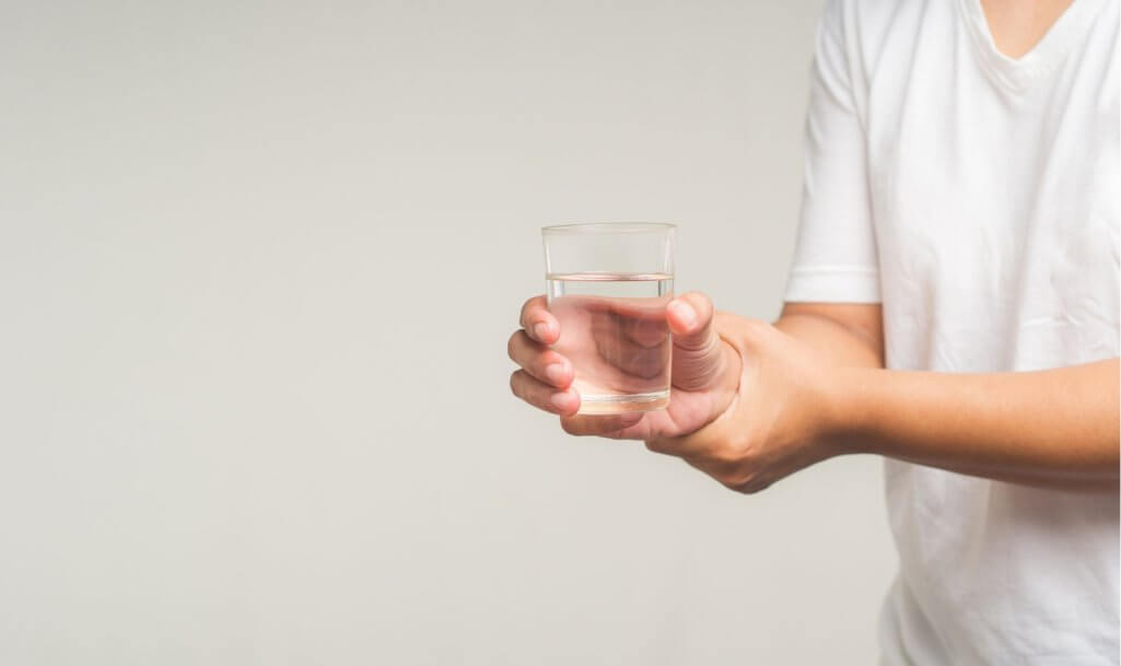 Close-up of hands trying to hold a glass of water. Causes of handshaking include Parkinson's disease, stroke, or brain injury. Mental health neurological disorder