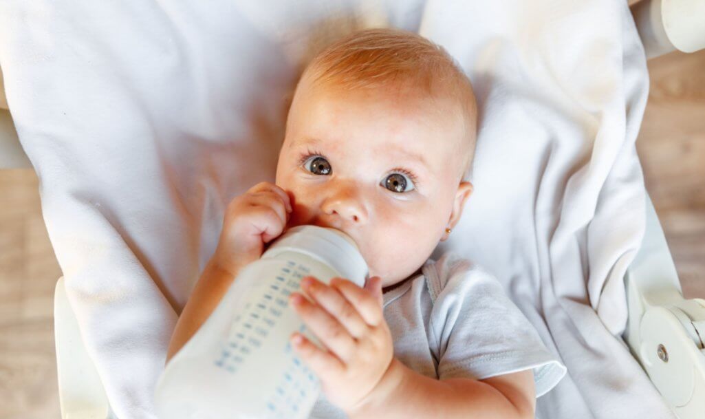 Cute little newborn girl drinking milk from bottle and looking at camera