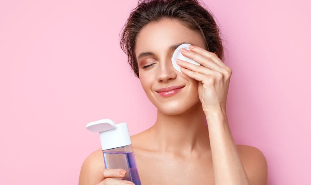 Woman removing makeup, holds cotton pads near face. Photo of woman with perfect skin on pink background. Beauty and skin care concept