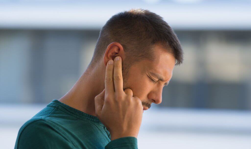 Man with tinnitus. Man touching his ear because of strong earache or ear pain.