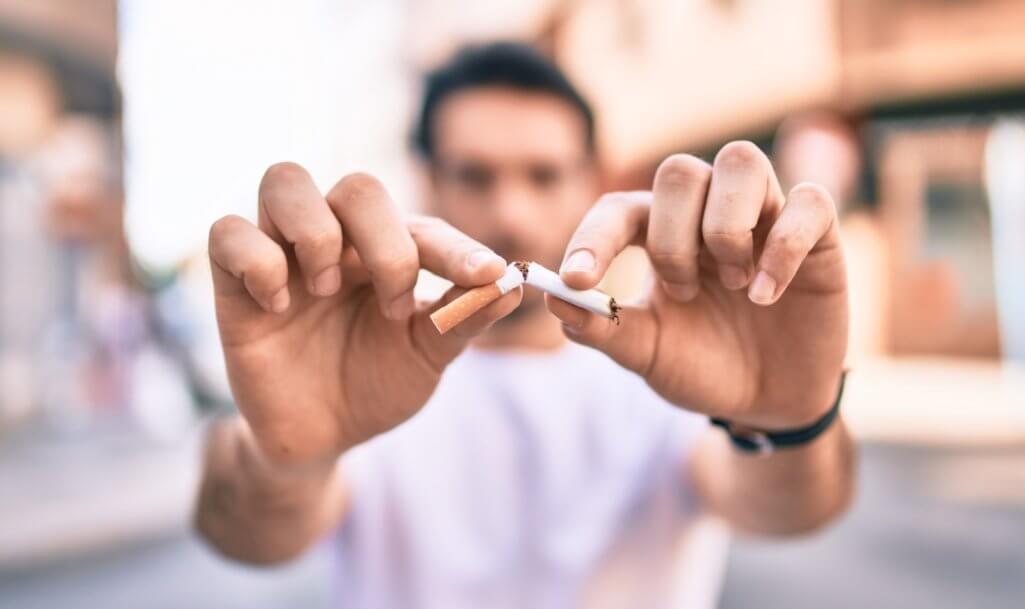 Young hispanic man breaking cigarette with hands walking at the city.