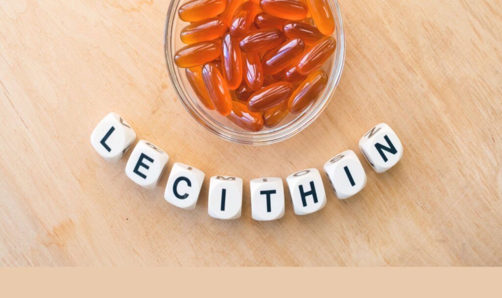 Lecithin gel pills in a round glass bowl and with the word Lecithin from the letters of cubes on a light wooden background.